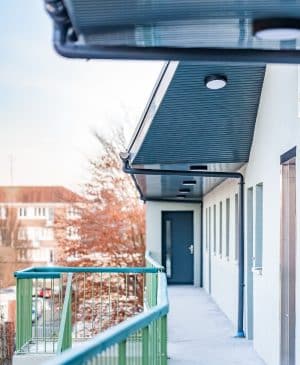 Image sur laquelle on voit un balcon aux rambardes vertes, en haut d'un immeuble qui semble faire peu d'étages. On aperçoit également le ciel bleu en toile de fond.