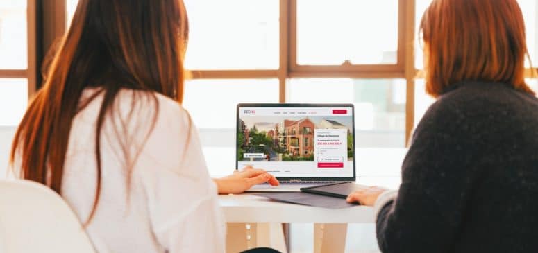 Photographie sur laquelle on voit deux femmes regarder dans la même direction. Elles regardent un ordinateur sur lequel on aperçoit le site internet du Groupe BECI.