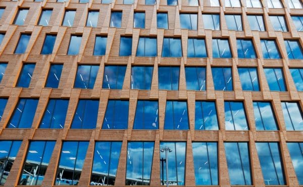 Photographie d'une façade d'immeuble ultra contemporain. Sur cet immeuble, les baies vitrées ont la part belle, et on aperçoit le ciel bleu dans celles-ci.